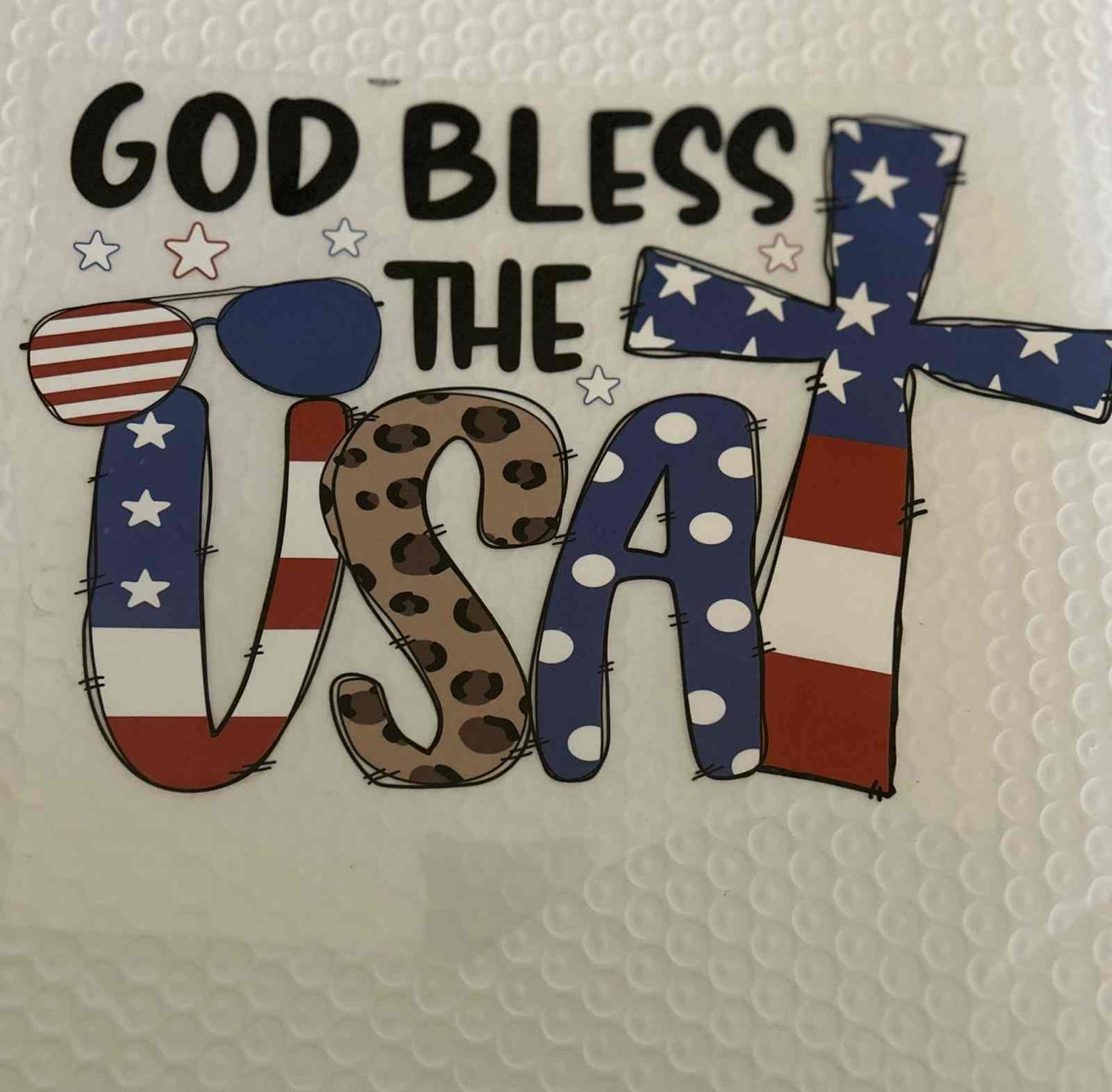 Patriotic design with &quot;God Bless the USA&quot; in flag-themed letters.