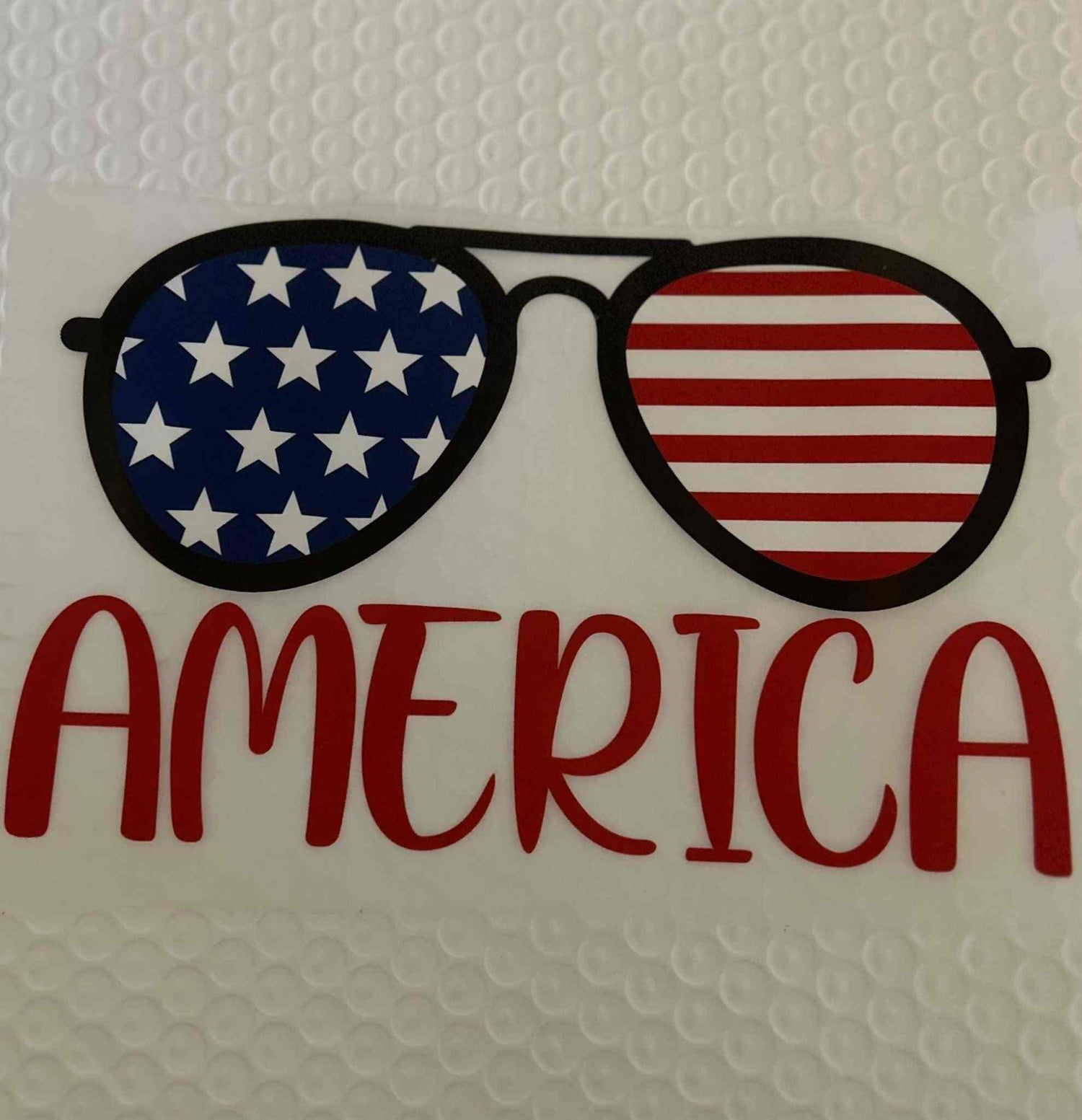 Patriotic design with sunglasses featuring American flag and &quot;America&quot; text.