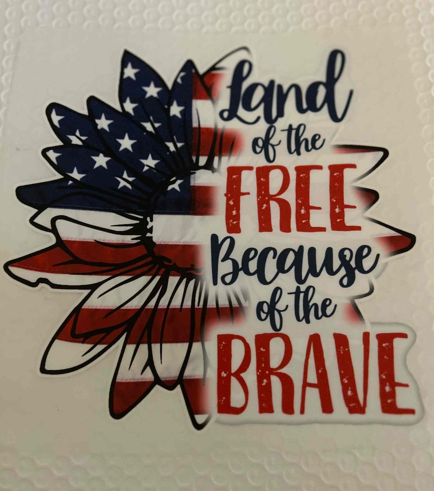 Patriotic Design sticker with &quot;Land of the Free Because of the Brave&quot; text and American flag motif.